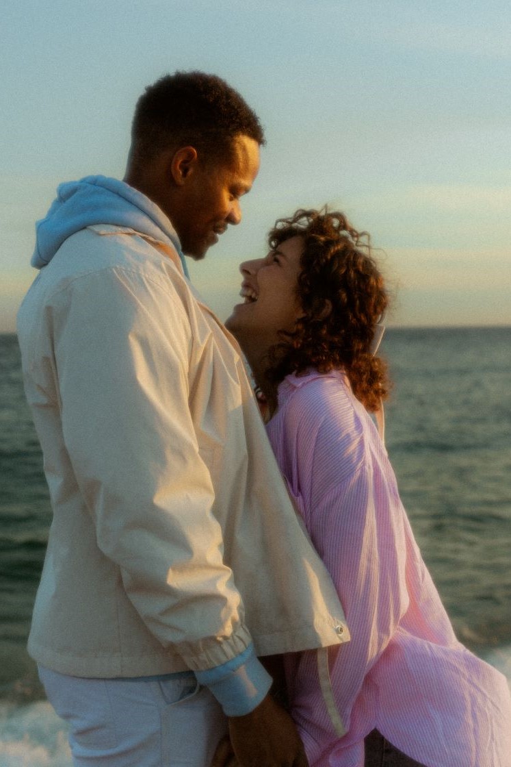Couple souriant se regardant dans les yeux devant la mer
