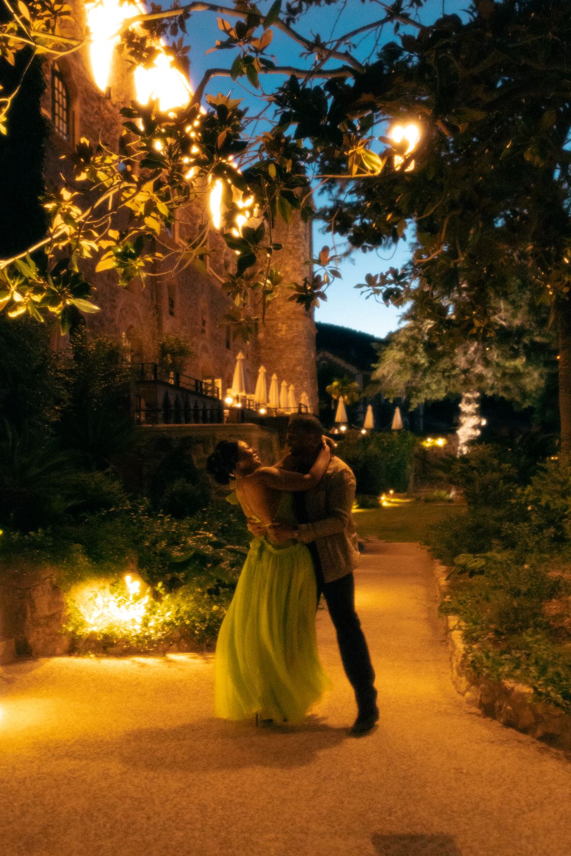 Couple sentrelacant devant un chateau entouré d'arbres, à la lumière orange